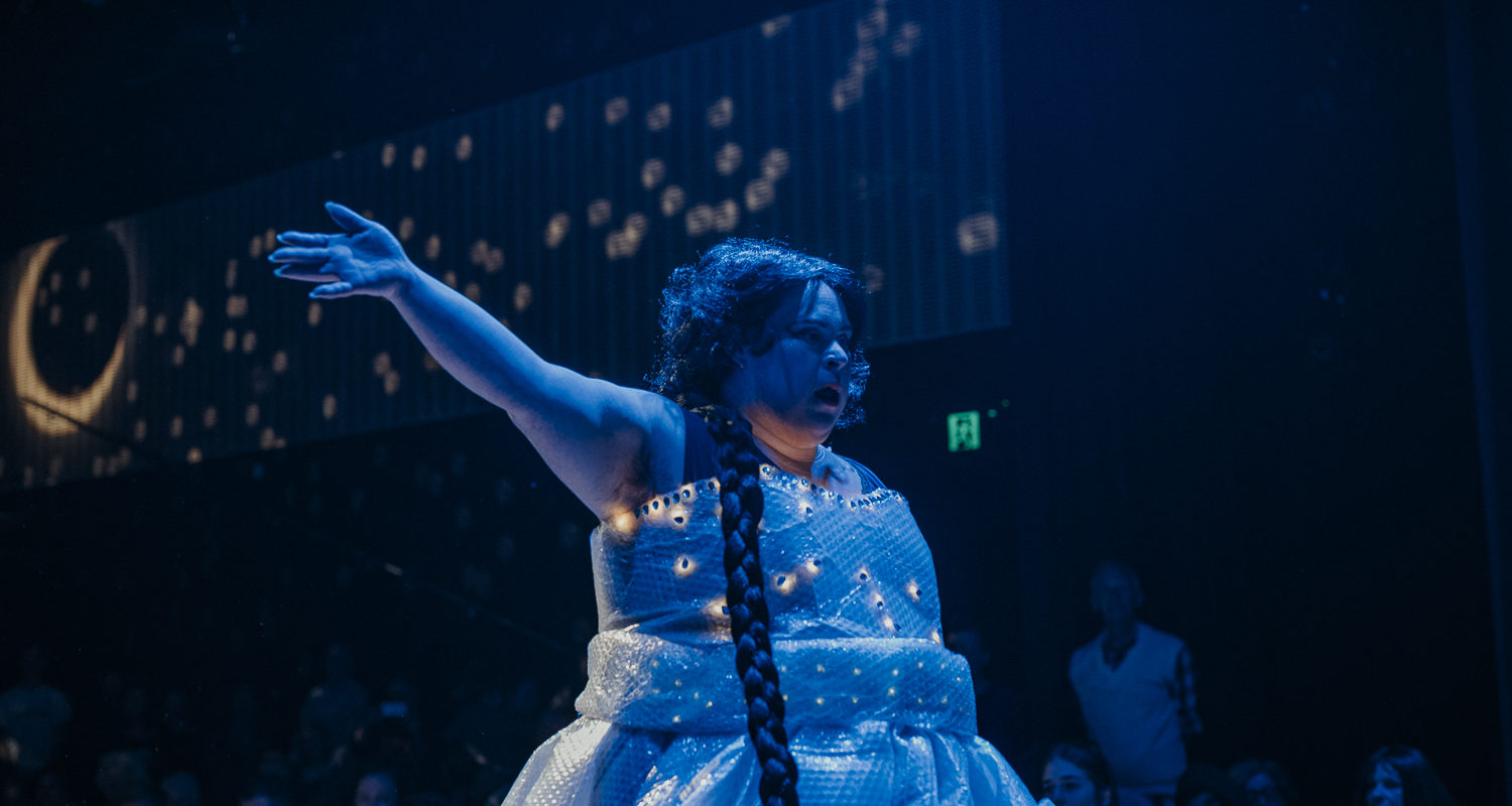 a woman is standing on a stage with her hand in the air.