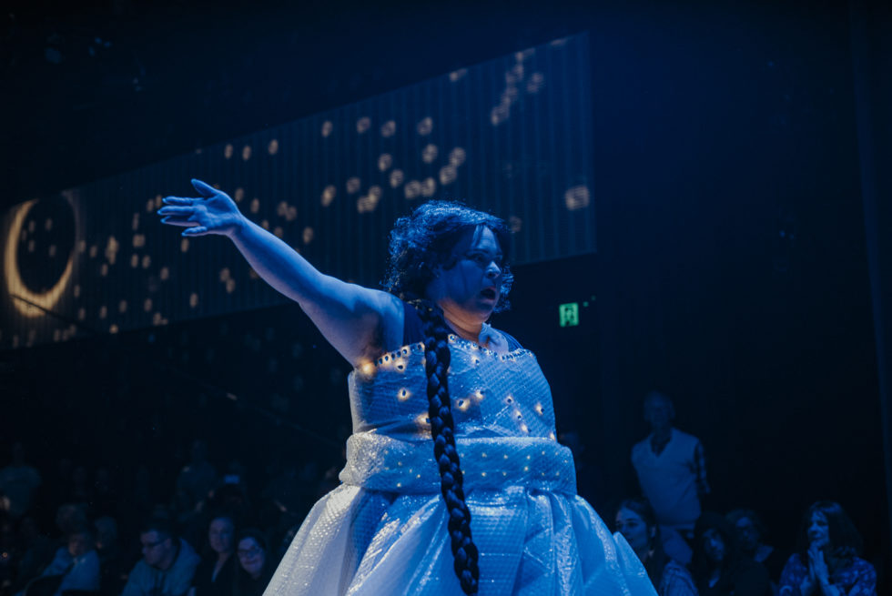 a woman is standing on a stage with her hand in the air.