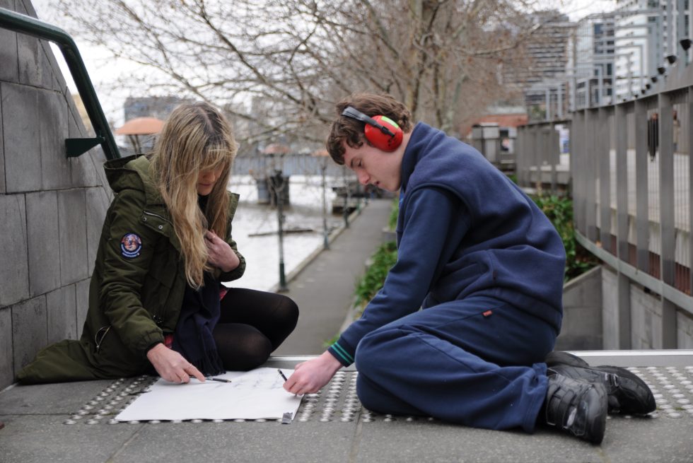 Two people are sitting on the steps taking rubbings.