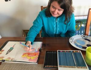 Emily sitting at their desk drawing with pencil colours on a piece of paper.