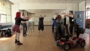 A group of people rehearsing with their hands up and in a circle.