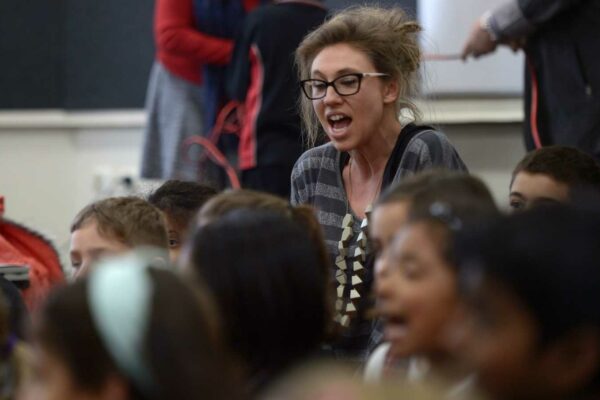 A photo of a person teaching in a classroom full of children.