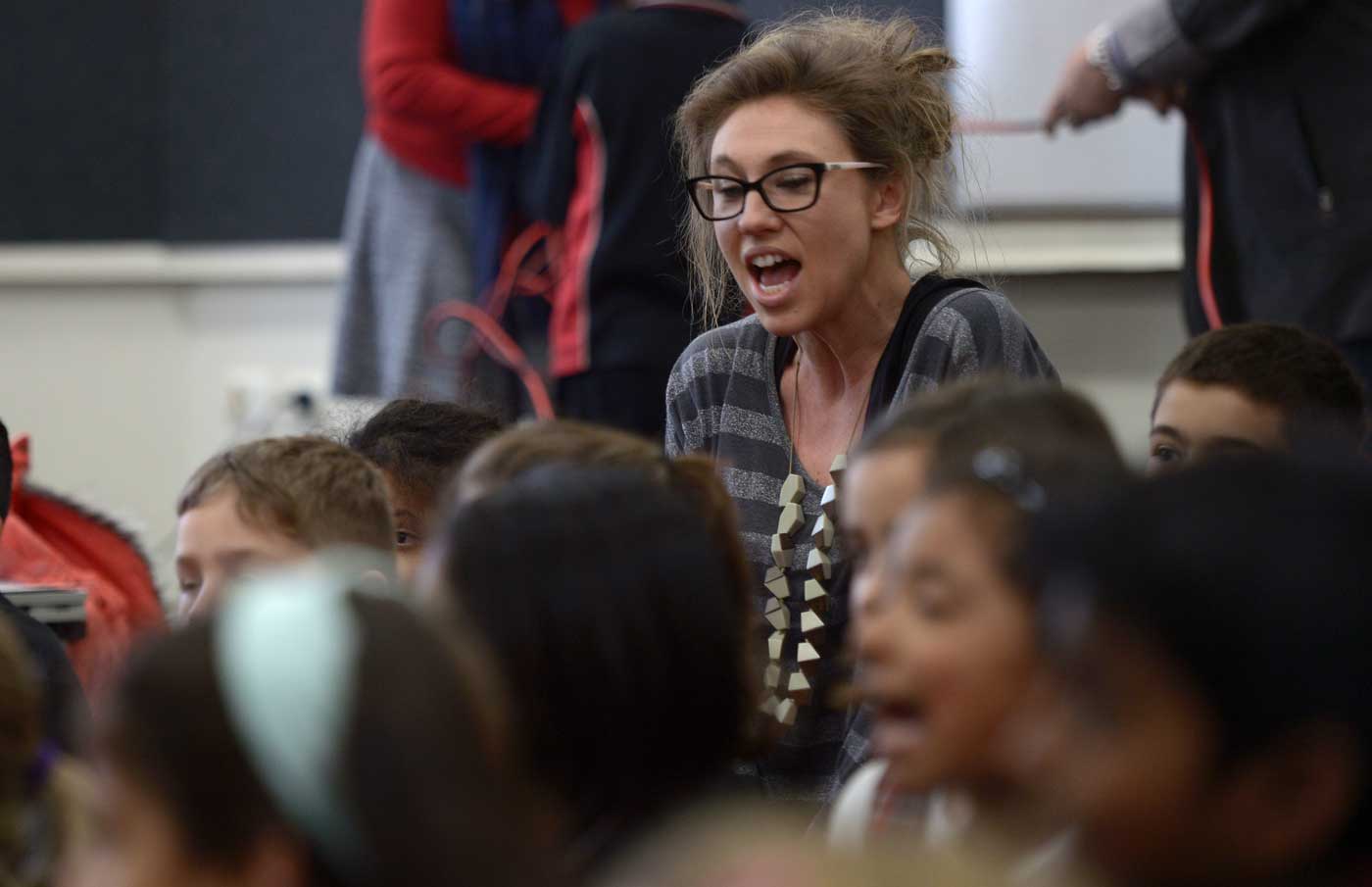 A photo of a person teaching in a classroom full of children.