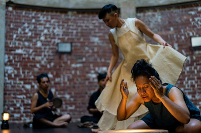 two woman are looking down at a light. there are people sitting against the brick wall in the background.