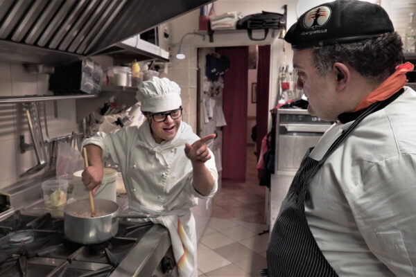 Two men are standing in a kitchen while one is pointing at the other.