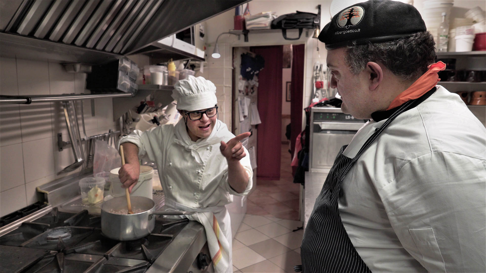 Two men are standing in a kitchen while one is pointing at the other.