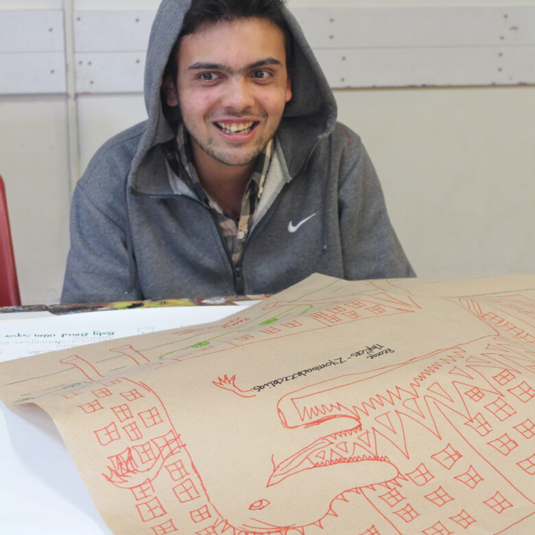 A man in a grey hoodie sits behind his artwork.