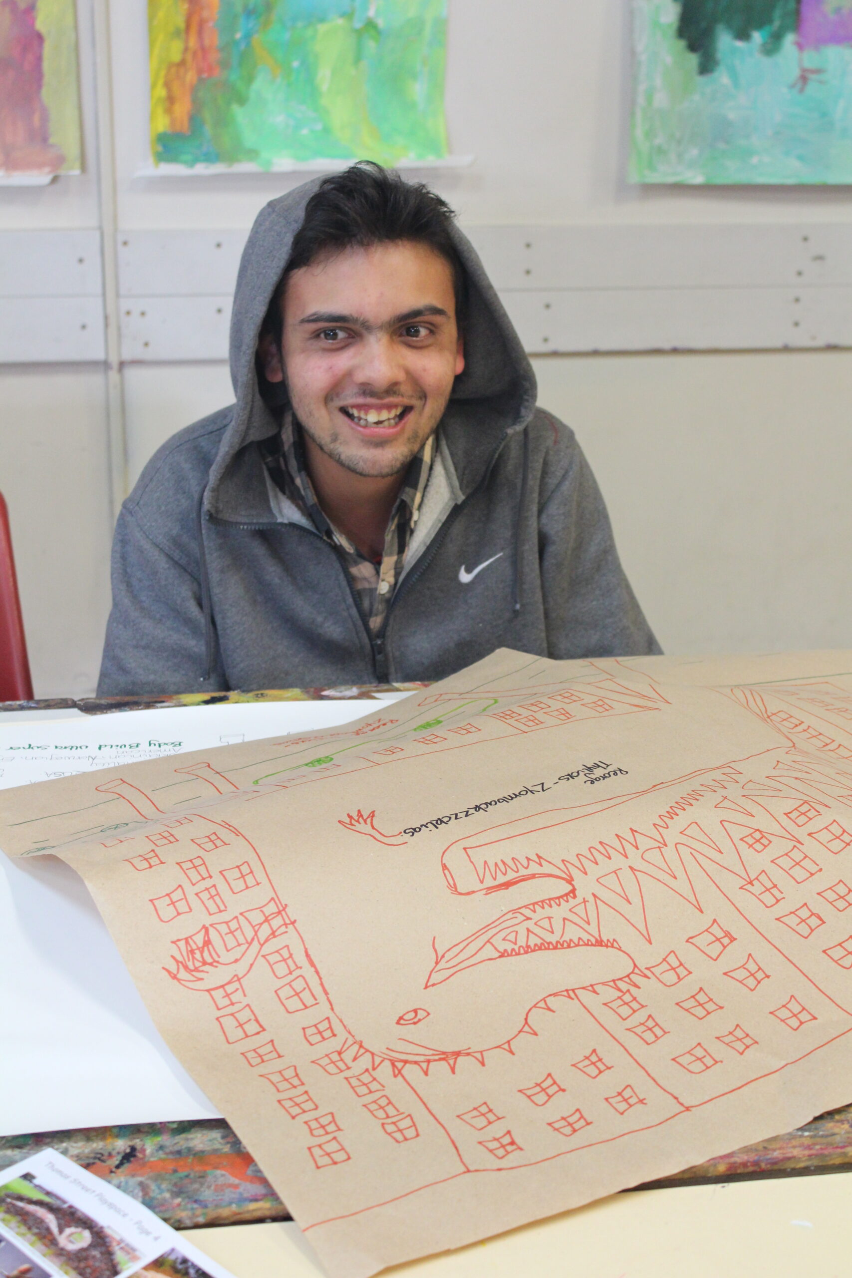 A man in a grey hoodie sits behind his artwork.