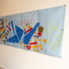 a banner of geometric blue shapes and red and yellow collaged with yellow, red and blue circles pinned to a white wall