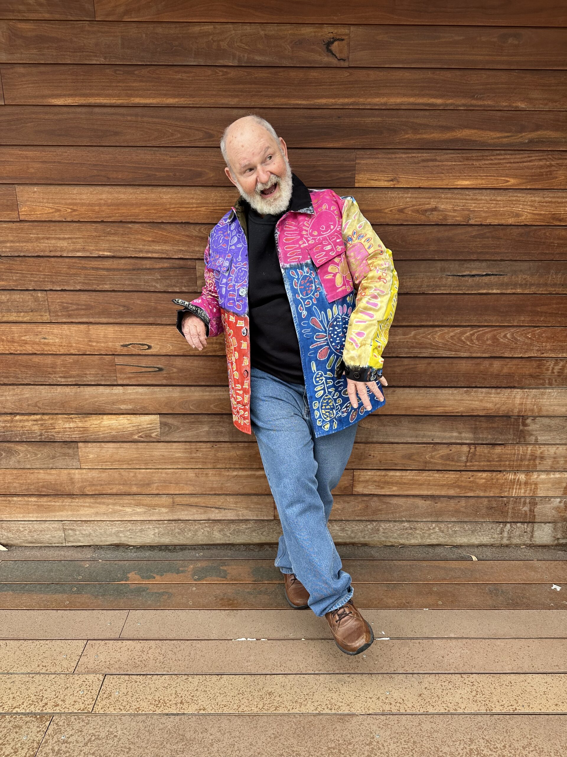 Robert Brown wears a hand painted colourful suit in front of a wooden wall.