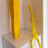 two yellow figures made from bright tape on a plinth, one seated with long legs, one is standing with short stout legs