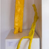 two yellow figures made from bright tape on a plinth, one seated with long legs, one is standing with short stout legs