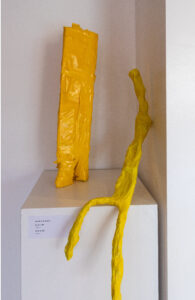 two yellow figures made from bright tape on a plinth, one seated with long legs, one is standing with short stout legs