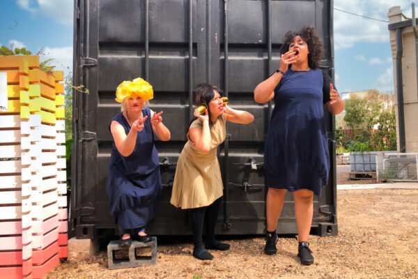 Performers Chelle Destefano, Zya Kane and Pearl Blackk performing in front of a shipping container. Chelle is signing the word see.