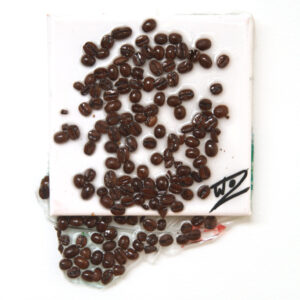 Coffee beans spill over a white canvas and leak off the square of the canvas in a viscous resin.