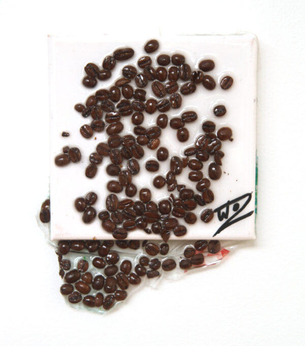 Coffee beans spill over a white canvas and leak off the square of the canvas in a viscous resin.