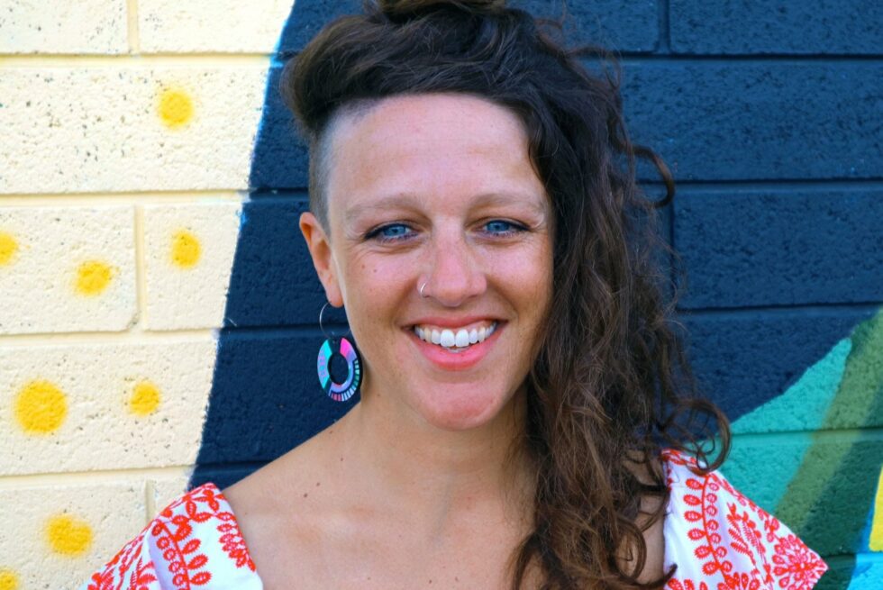 Andi Snelling smiling at the camera against a colourful brick wall.