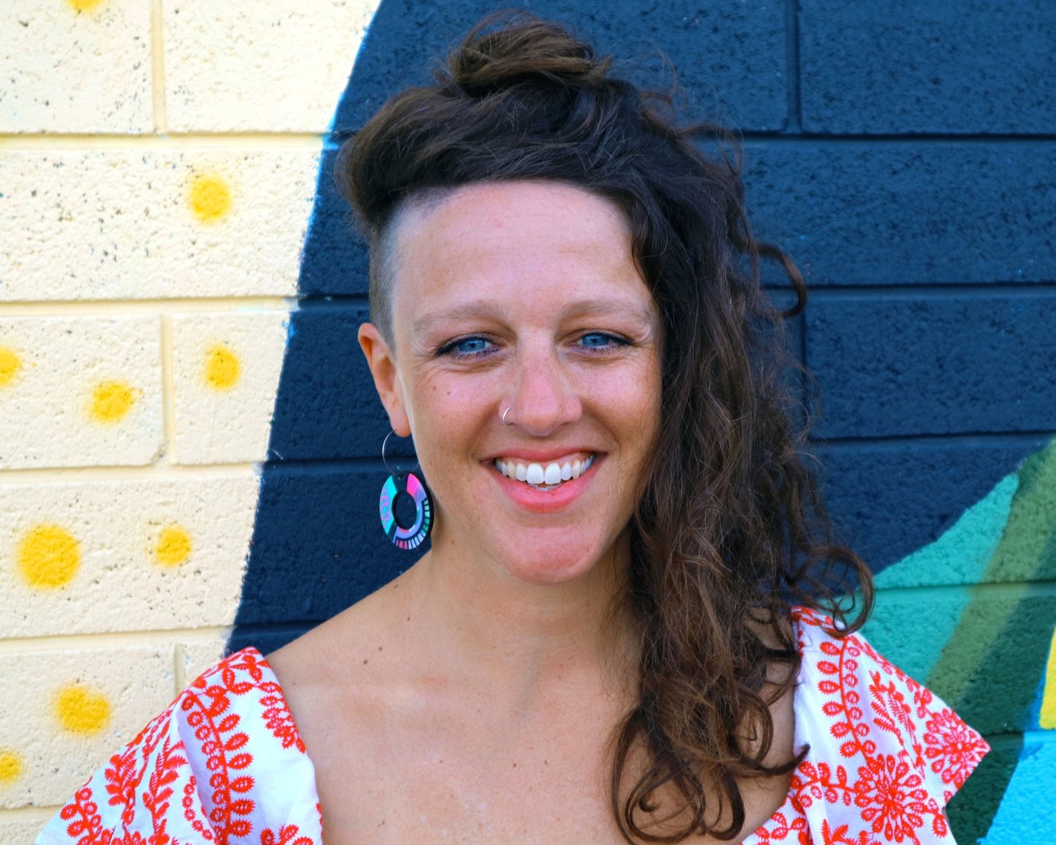 Andi Snelling smiling at the camera against a colourful brick wall.