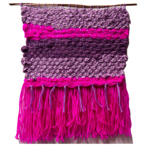 A weaving done with wool. It has pink, purple and mauve stripes with bright pink tassels.