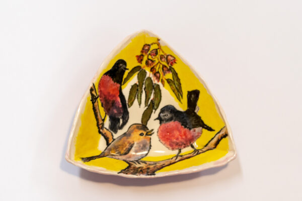 A ceramic bowl showing three pink Robbins dance on a branch.