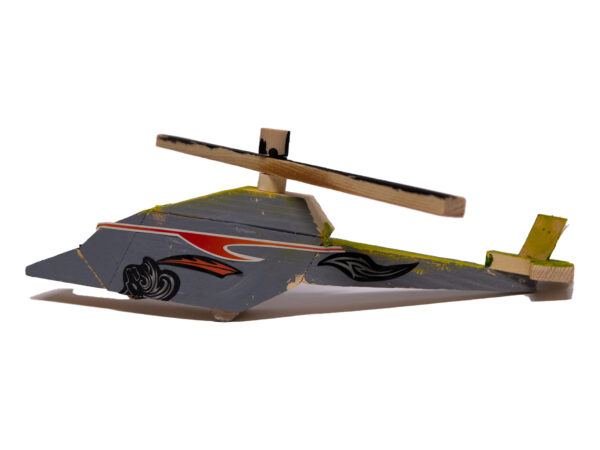 Small model of a helicopter made from wood. The body is painted grey with a red sticker like an upside-down wave across the cockpit area. Below there is a sticker of black swirls. The propeller has been left bare with a touch of black paint on the top.