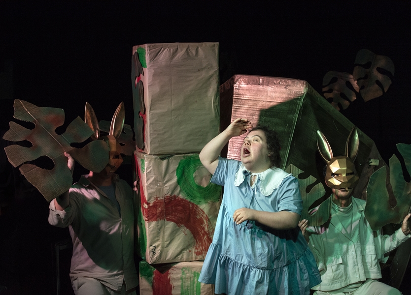 A person is standing infant of fabric boxes, while people in bunny masks wave banana leaves.