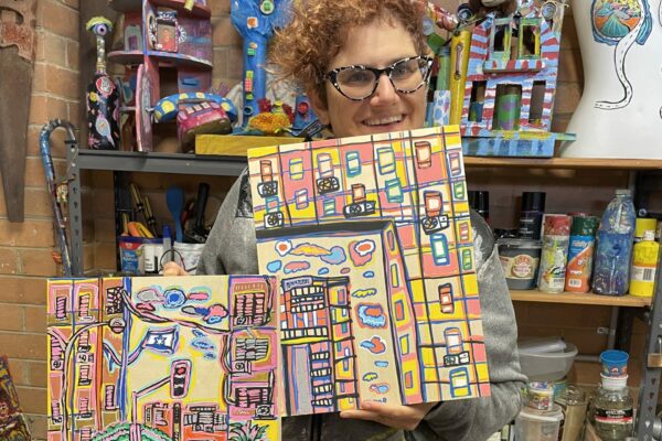 Tamar in her studio holding 2 artworks