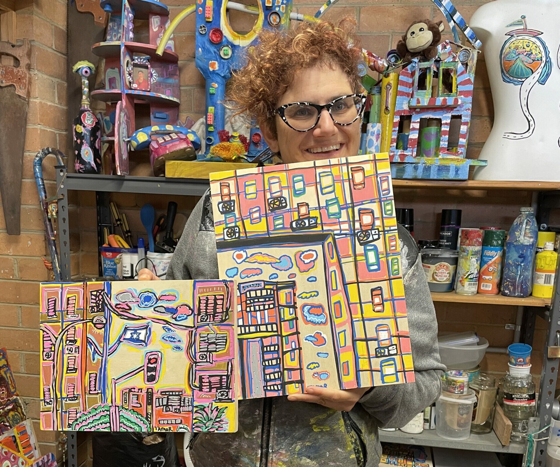 Tamar in her studio holding 2 artworks