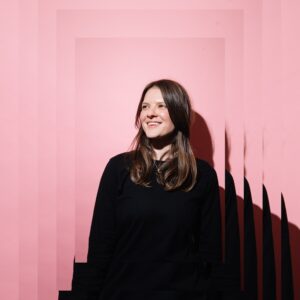 A2 photograph of a woman with a pink background smiling. The Image is on one rectangle in the middle with four increasing rectangular frames behind it, the image is layered on itself giving the image a sense of depth.
