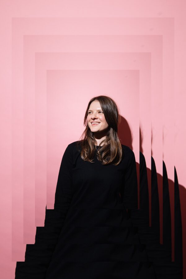 A2 photograph of a woman with a pink background smiling. The Image is on one rectangle in the middle with four increasing rectangular frames behind it, the image is layered on itself giving the image a sense of depth.