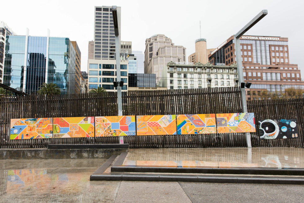 A painted mural is on top of a wooden fence overlooking the Melbourne city skyline