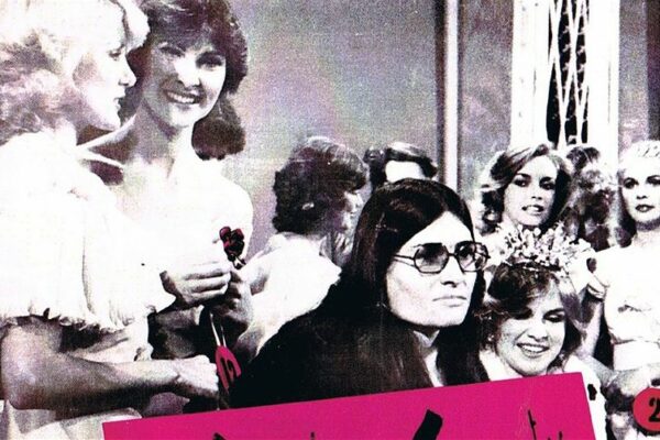 Lesley Hall on stage at Beauty Quest 1981 surrounded by contestants holding a protest sign