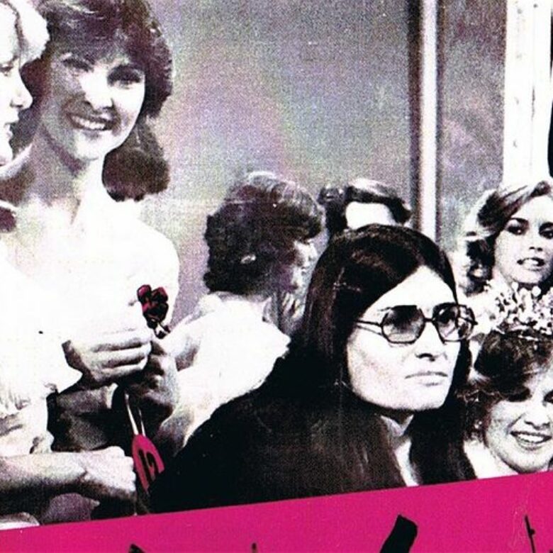 Lesley Hall on stage at Beauty Quest 1981 surrounded by contestants holding a protest sign