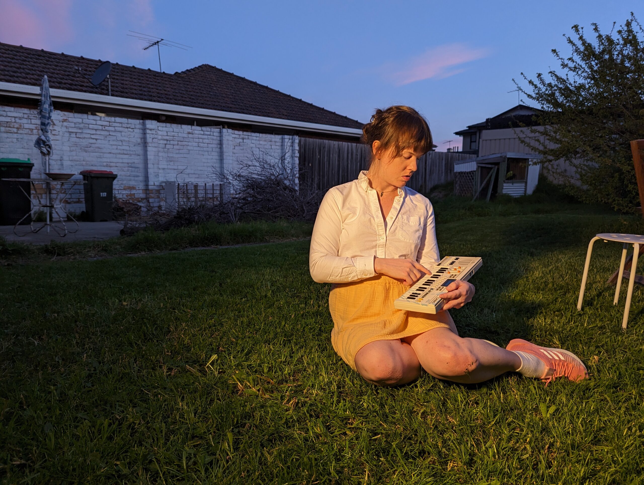 Katie Dey sits on the lawn holding a small keyboard.