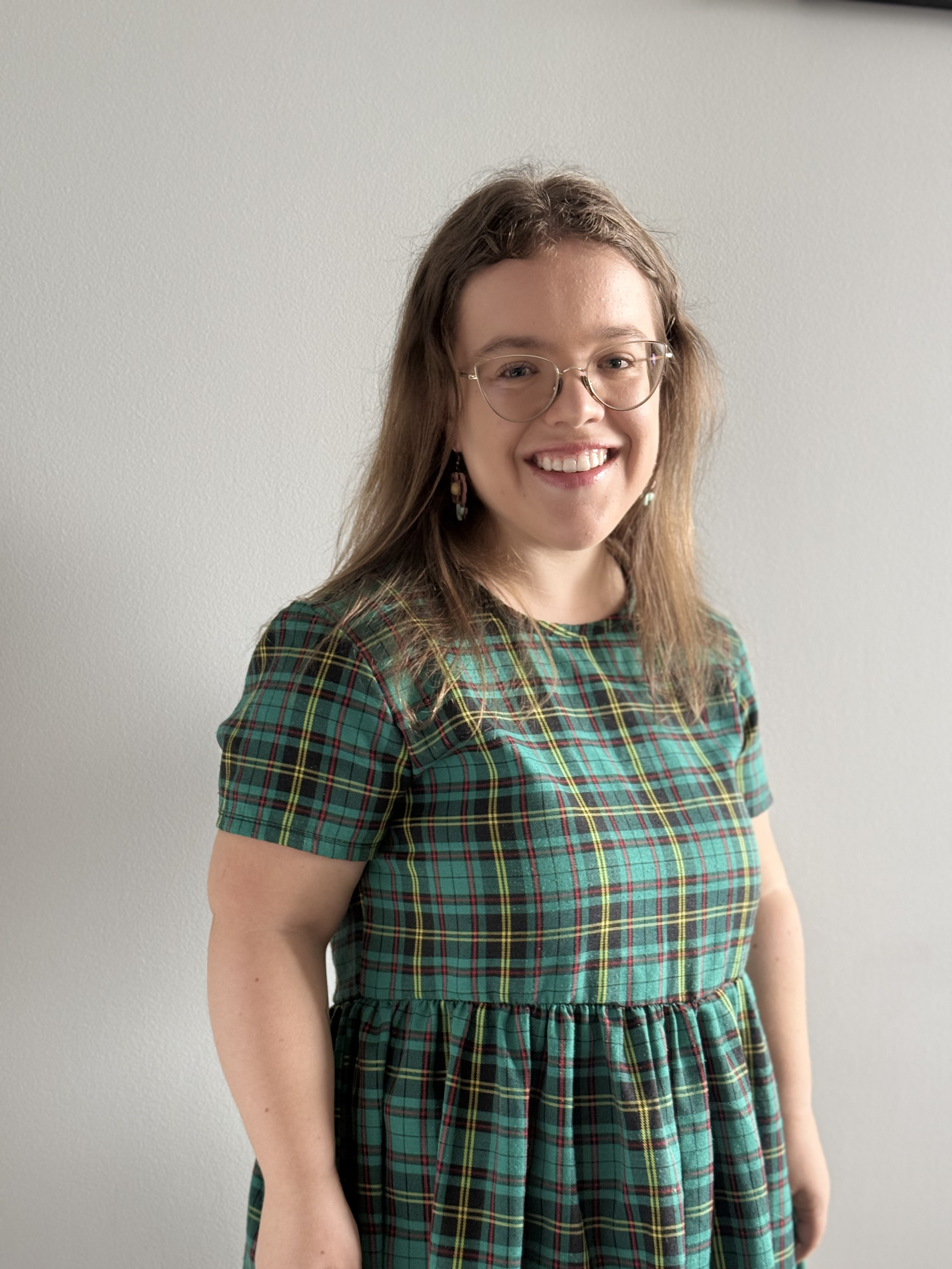 A person of short stature with glasses wearing a plaid green dress.