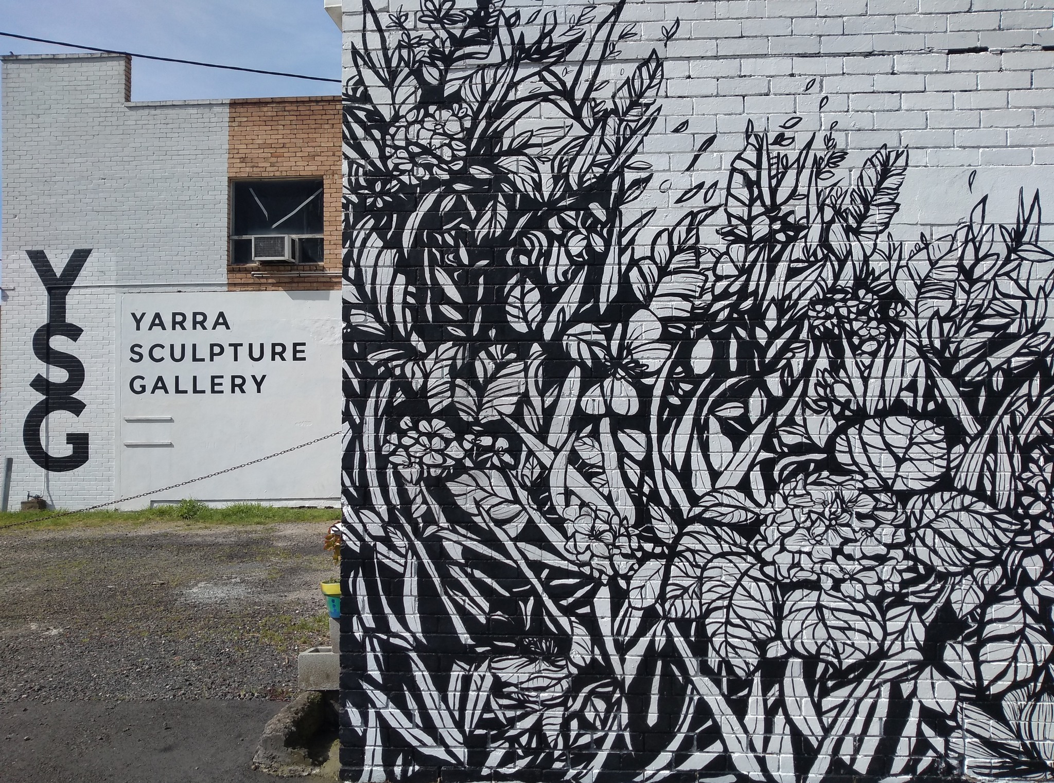 A photo outside the Yarra Sculpture Gallery. There is a beautiful mural by Manda Lane on a brick wall with black and white floral and plant illustration