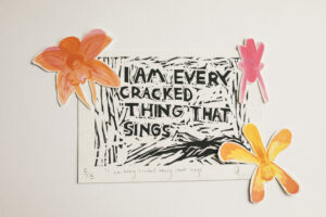 Linocut print in black ink of a text saying ‘I am every cracked thing that sings’. There is an orange watercolour flower on the top left side of the frame. There are pink and yellow flowers on the right side.