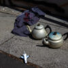 Two teapots, a toy plane and a rag with paint on them sitting on a broken footpath