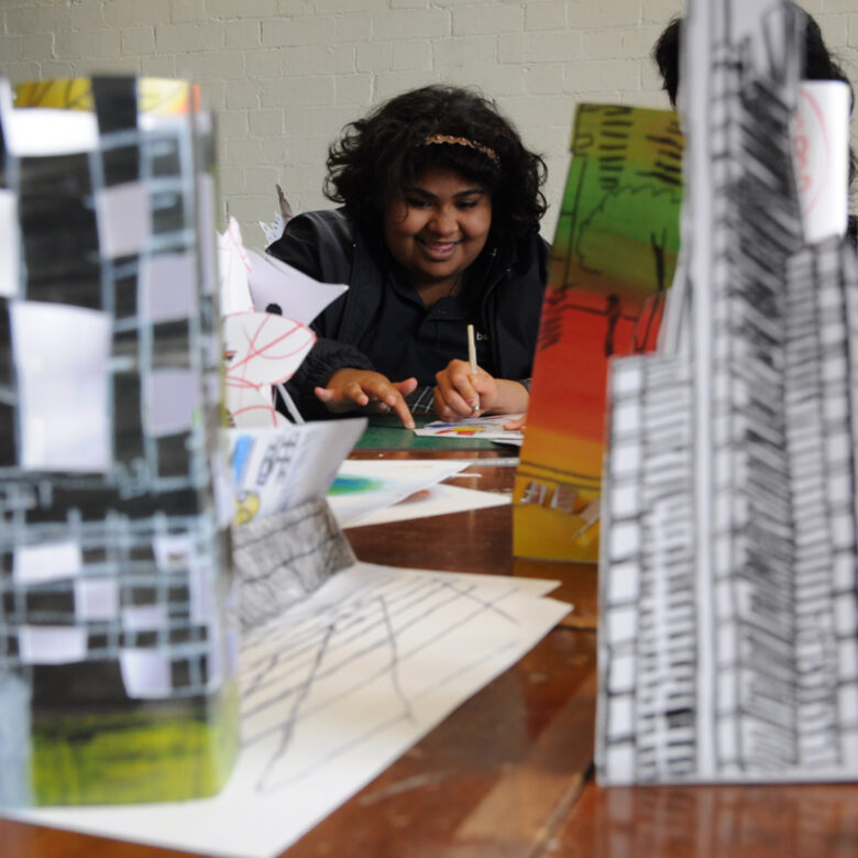 A person looking between paper models of buildings and skyscrapers.