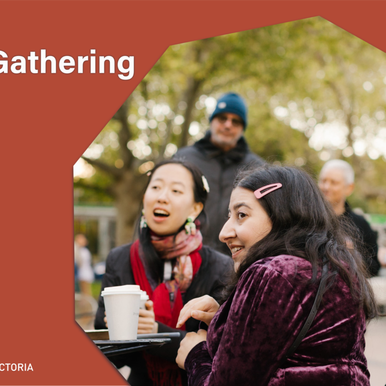2 people sit at a table with others gathered behind.