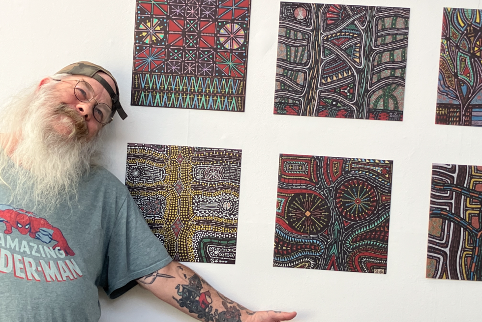 A person with arm stretched out in front of their artwork proudly.