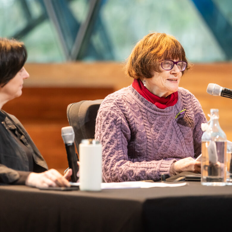 Two people seated at a table with microphones presenting a workshop.