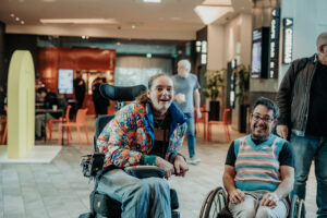 Two people in wheelchairs smiling at ACMI.