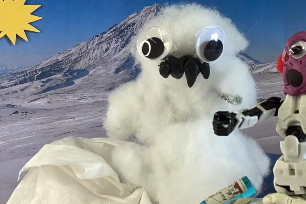 A snowman is in front of snowy mountains with his friend.
