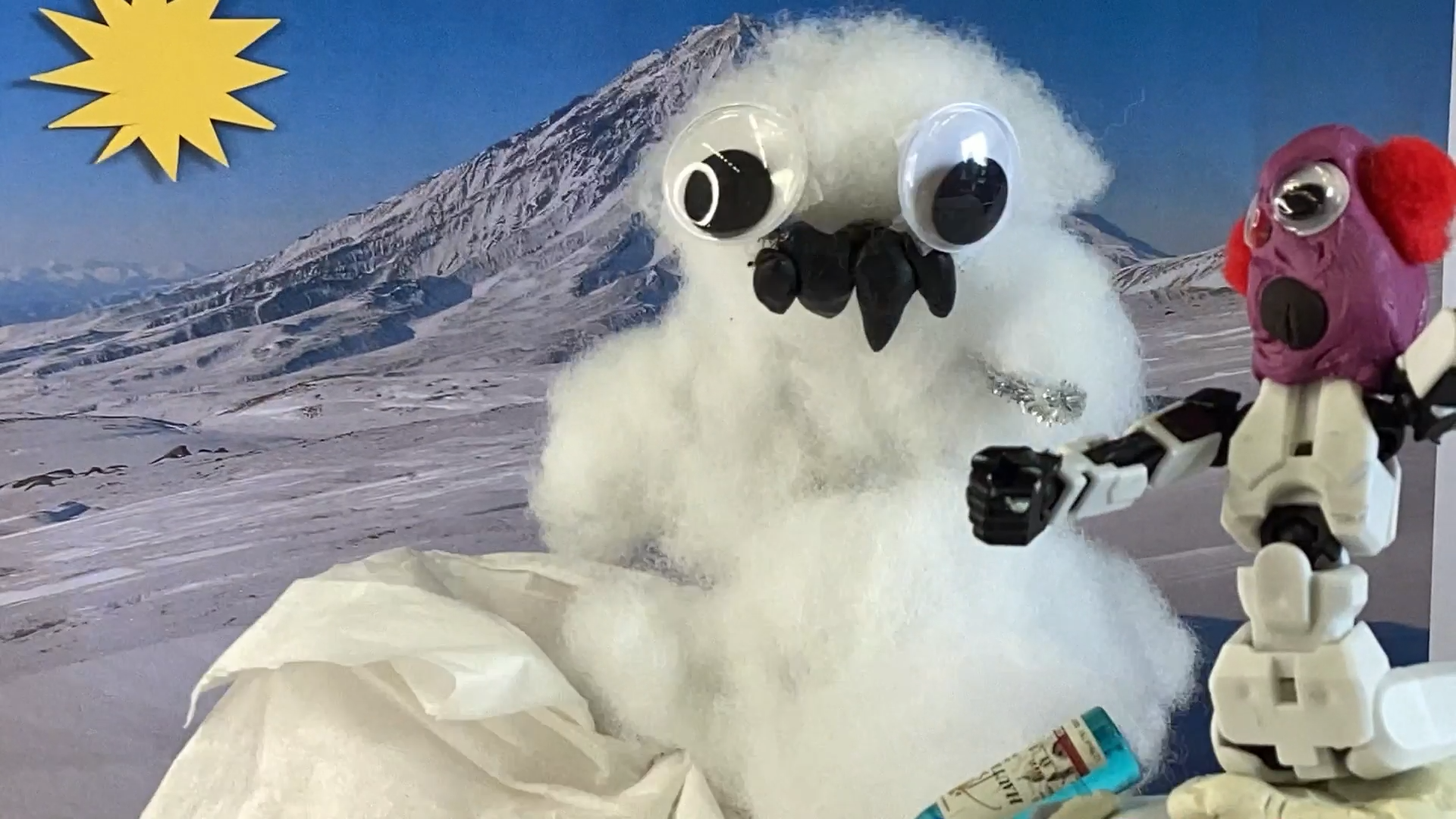 A snowman is in front of snowy mountains with his friend.