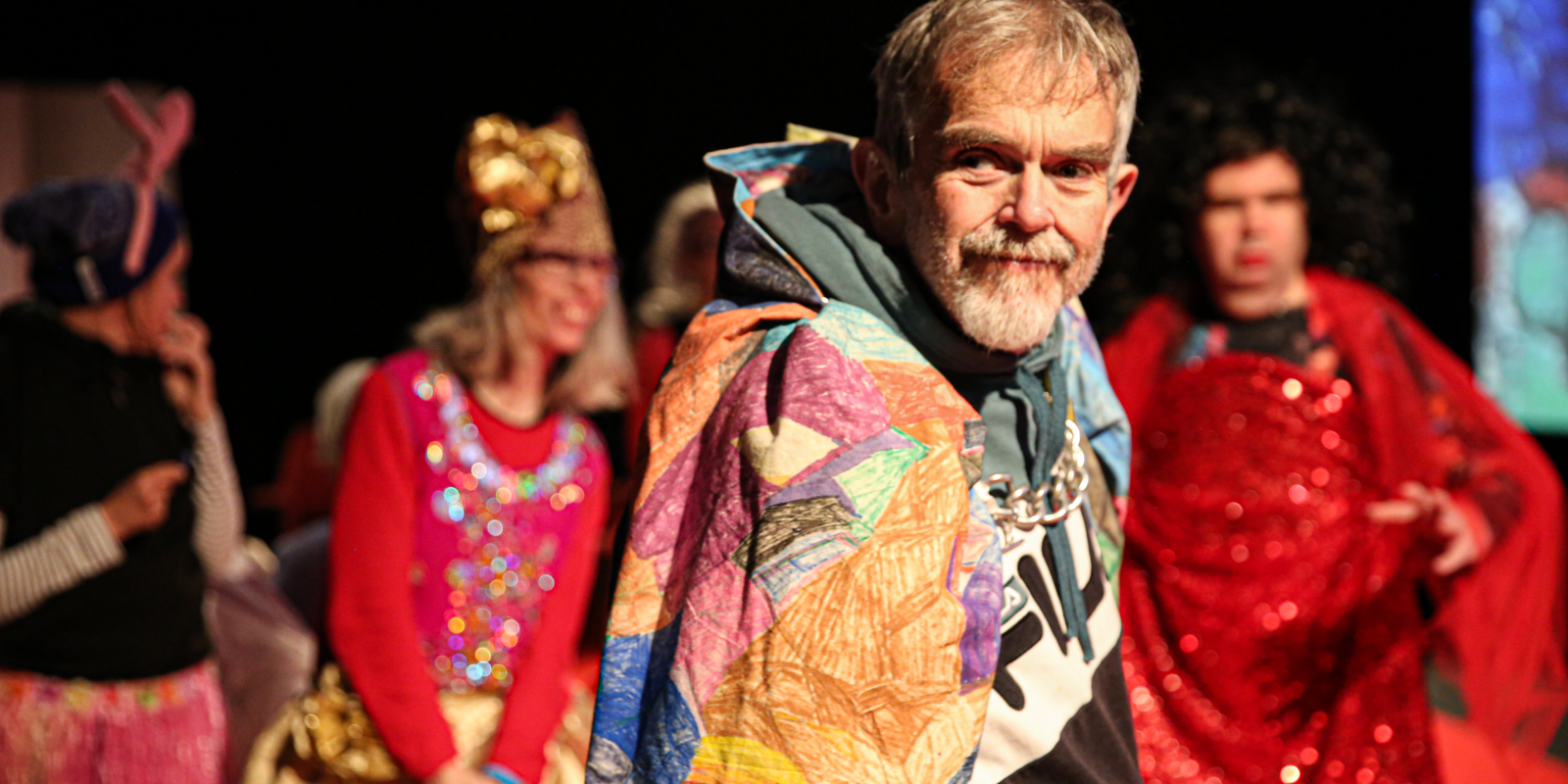 A person wearing a colourful cape with others in the background.
