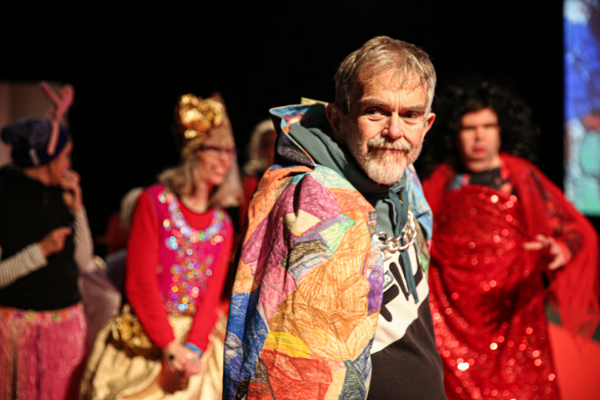 A person wearing a colourful cape with others in the background.