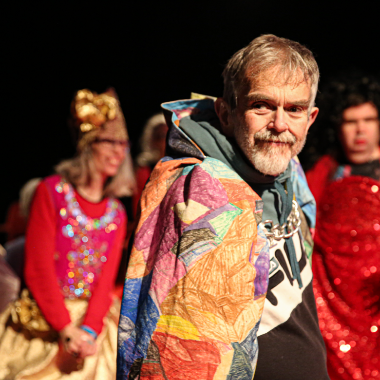 A person wearing a colourful cape with others in the background.