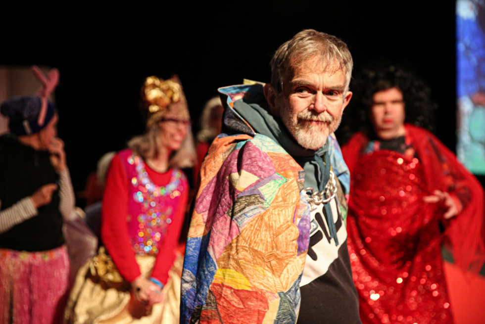 A person wearing a colourful cape with others in the background.