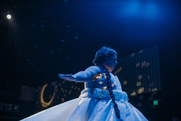 A person in a dress on stage under blue lights.